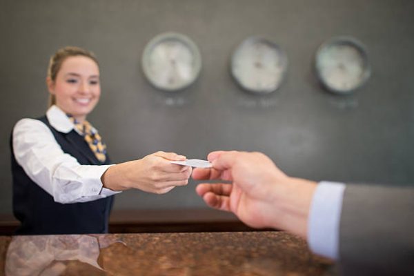 Woman working at a hotel handing a loyalty card or card key at the front desk