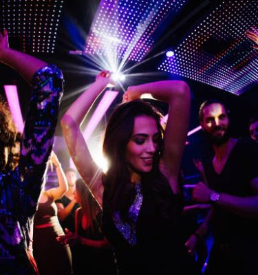 Young women dancing happily with her friends in a nigh club party with disco lights